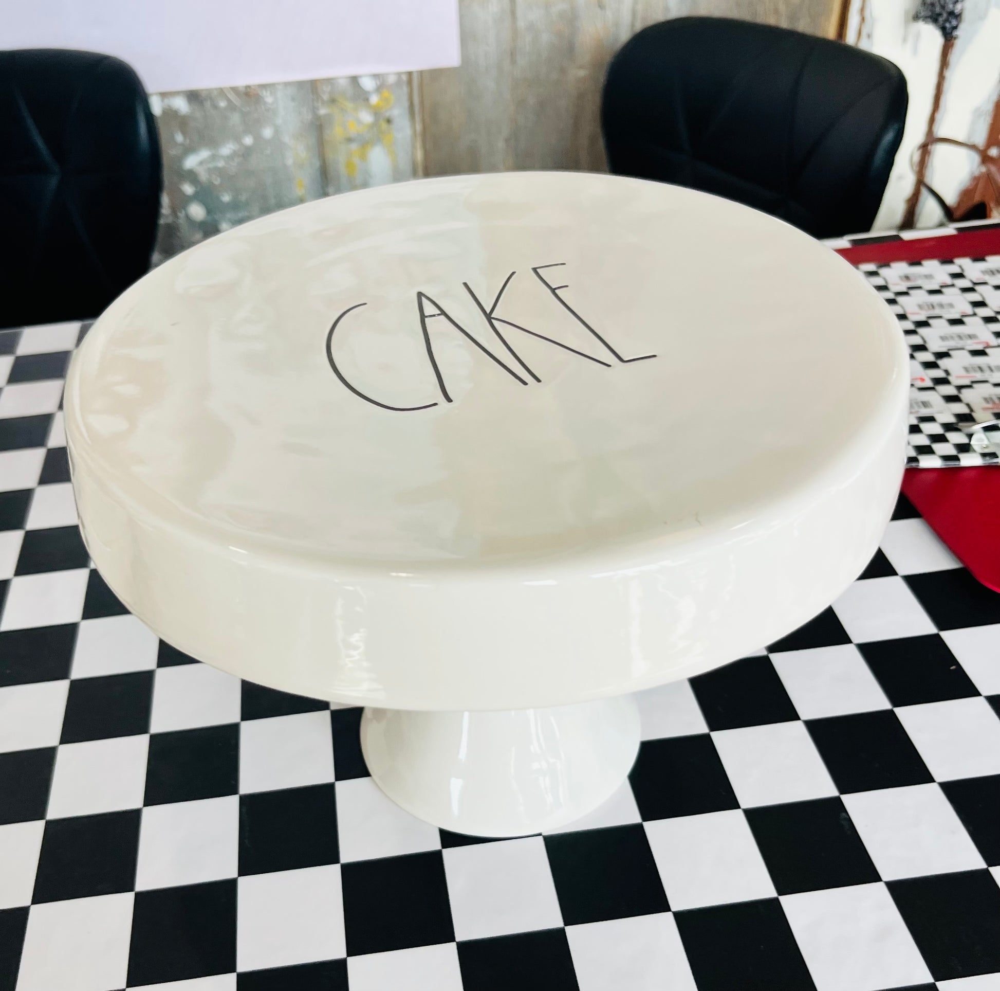 White cake stand with 'CAKE' text on a checkered floor