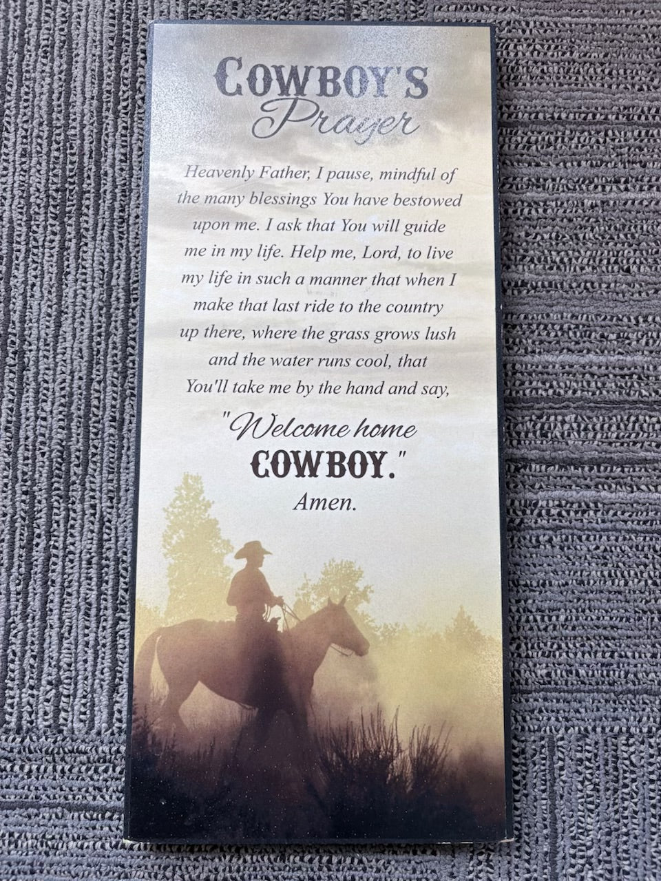 A printed "Cowboy's Prayer" with a sepia-toned cowboy silhouette and prayer text, photographed on a gray textured fabric background.