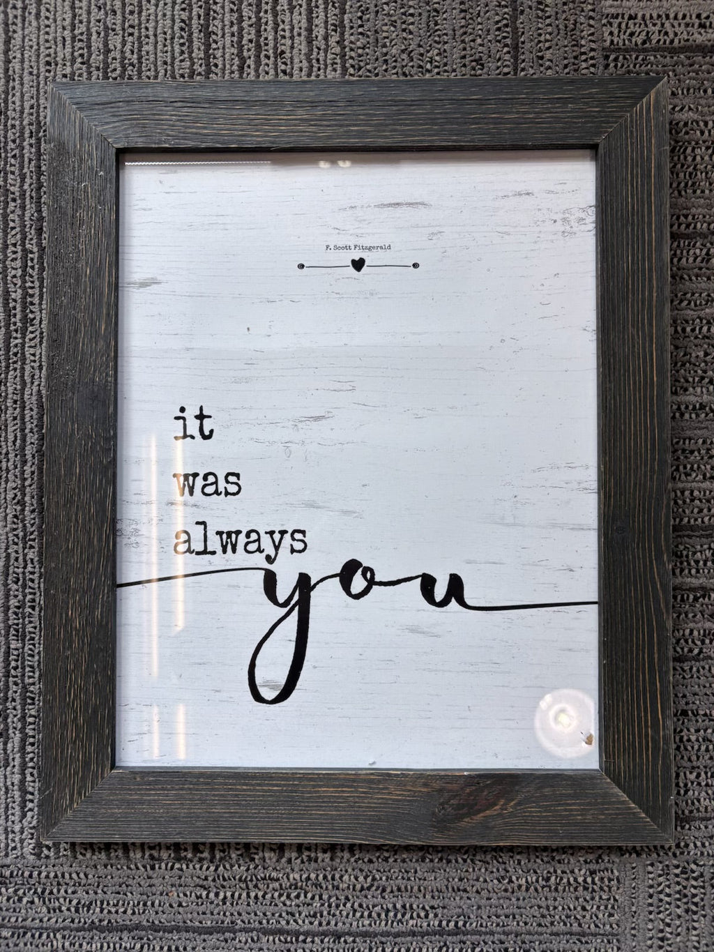 A framed rustic wall art print with a dark brown wood frame, featuring the phrase 'it was always you' in black typography on a distressed white background, mounted on a textured gray wall.