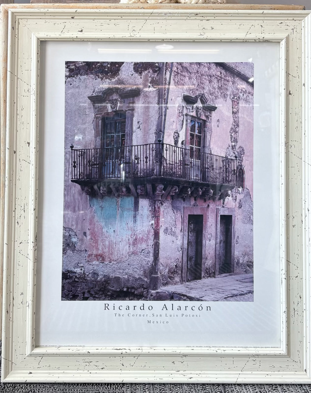 A framed art print featuring a photograph of a weathered building facade with balconies and doors, signed 'Ricardo Alarcón' and labeled 'The Cactus, San Luis Potosíno, Mexico.' The print is matted in white and housed in a distressed off-white wooden frame.