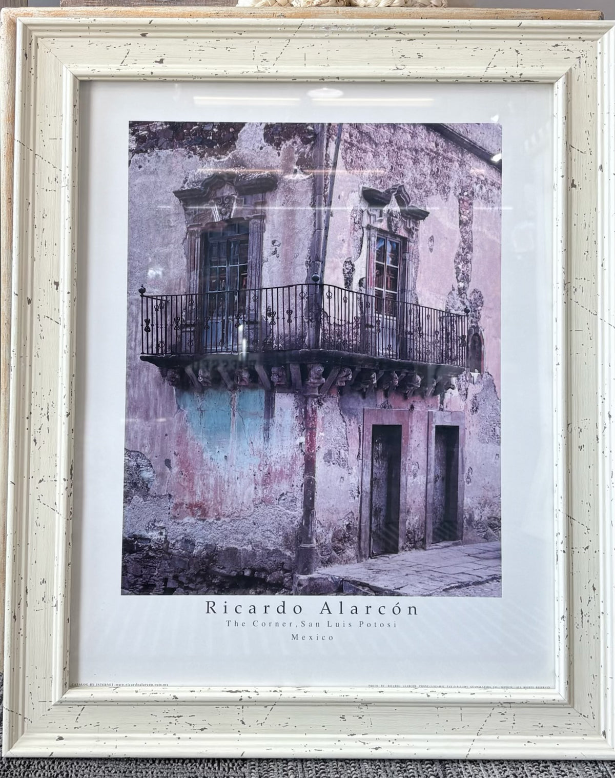 A framed art print featuring a photograph of a weathered building facade with balconies and doors, signed 'Ricardo Alarcón' and labeled 'The Cactus, San Luis Potosíno, Mexico.' The print is matted in white and housed in a distressed off-white wooden frame.